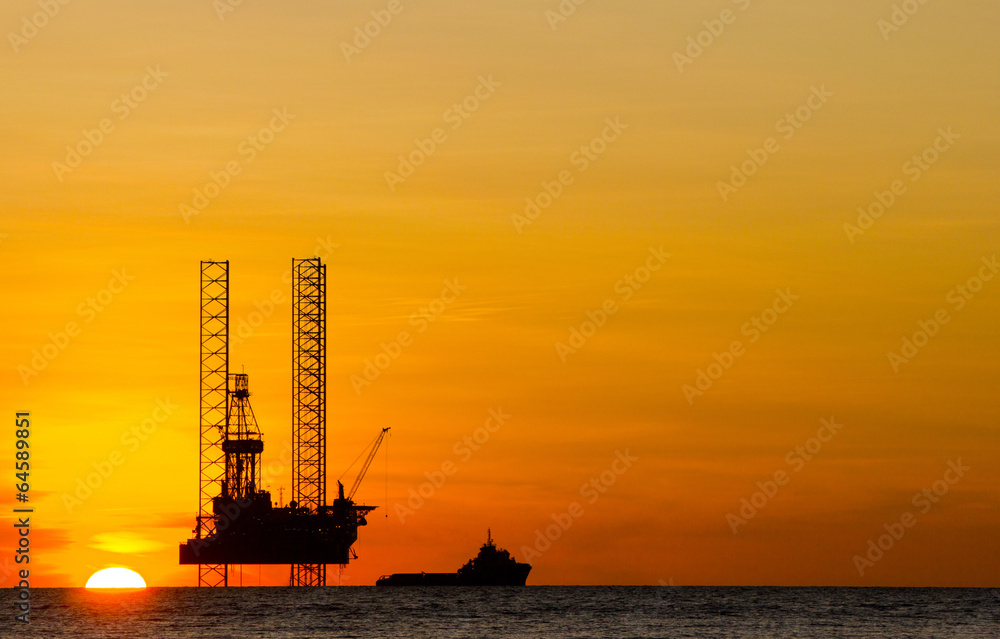 Offshore drilling rig and supply vessel at sunset