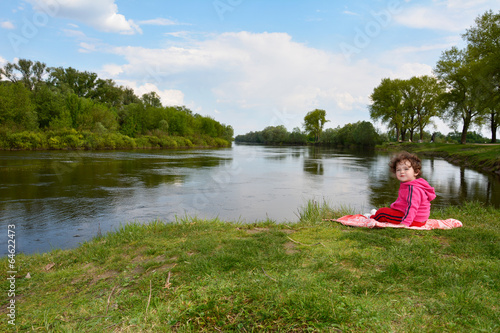 Little girl sitting near the river. © tsomka