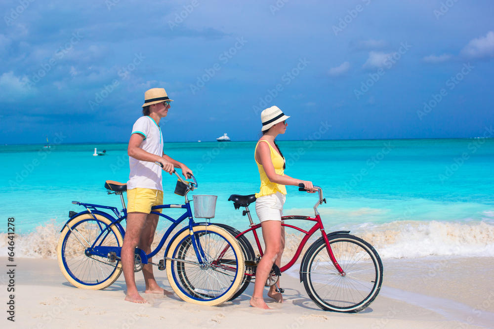 Fototapeta premium Young happy couple riding bikes on white tropical beach