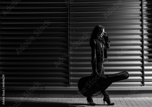 young woman in black jacket with guitar at night station