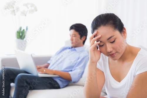 Upset woman sitting on couch while boyfriend uses laptop