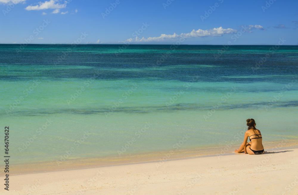 Young woman sitting alone on a sandy beach Young woman sitting alone on a sandy beach
