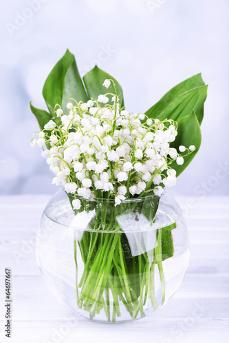 Beautiful lilies of the valley in glass vase on wooden table