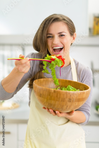 Portrait of happy young housewife tasting salad in kitchen