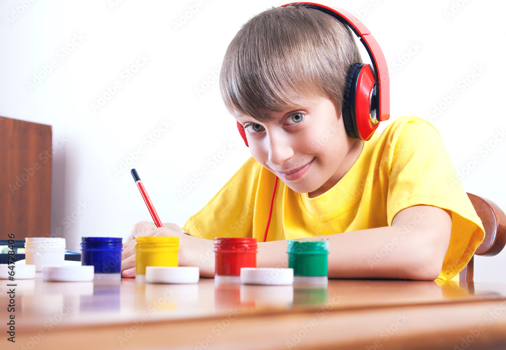 Beautiful happy child with headphones sitting at table painting Beautiful happy child with headphones sitting at table painting