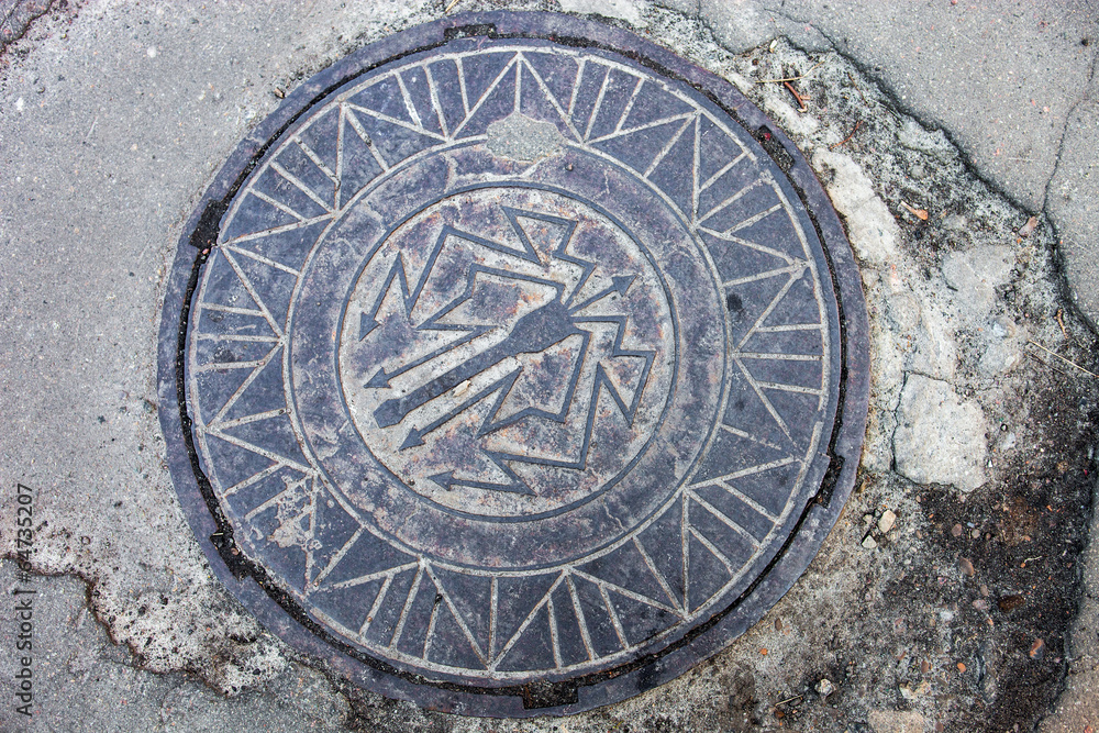 Manhole with metal cover in the cracked asphalt surface