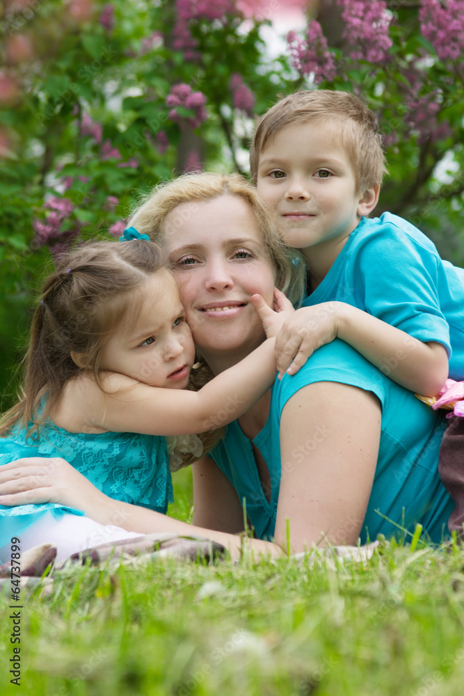 Mother and two children hugging among green grass Mother and two children hugging among green grass