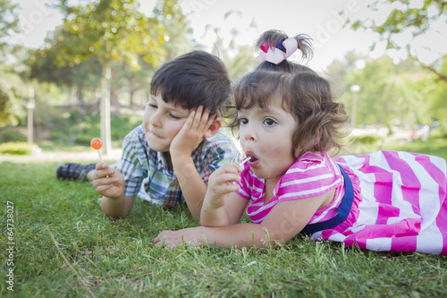 Young Brother and Baby Sister Enjoying Their Lollipops Outdoors