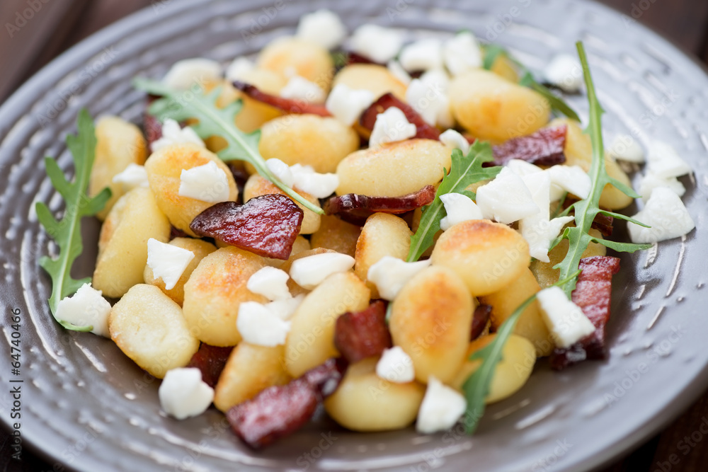 Roasted gnocchi with cheese, meat and arugula, close-up Roasted gnocchi with cheese, meat and arugula, close-up