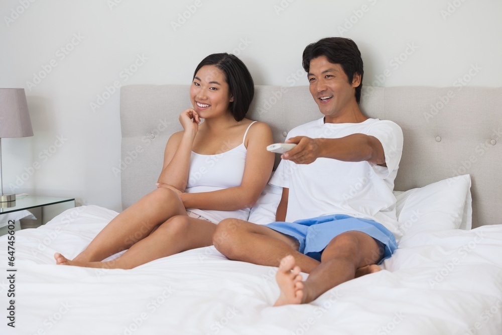 Happy couple lying on bed together watching tv Happy couple lying on bed together watching tv