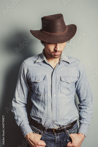 Cowboy standing by a blue wall © LoloStock