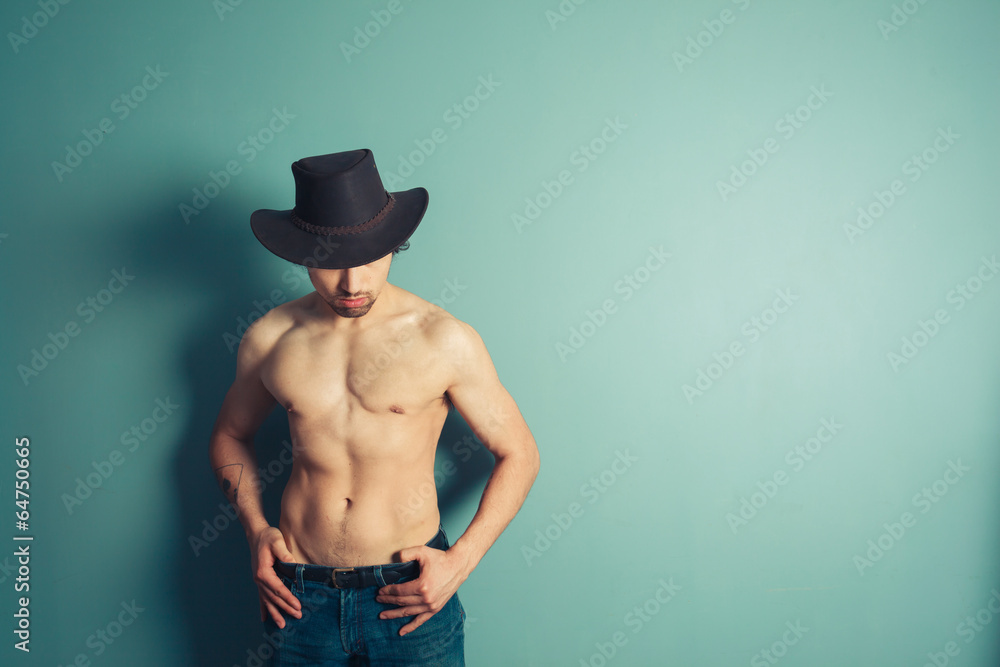 Shirtless cowboy striking a pose by blue wall