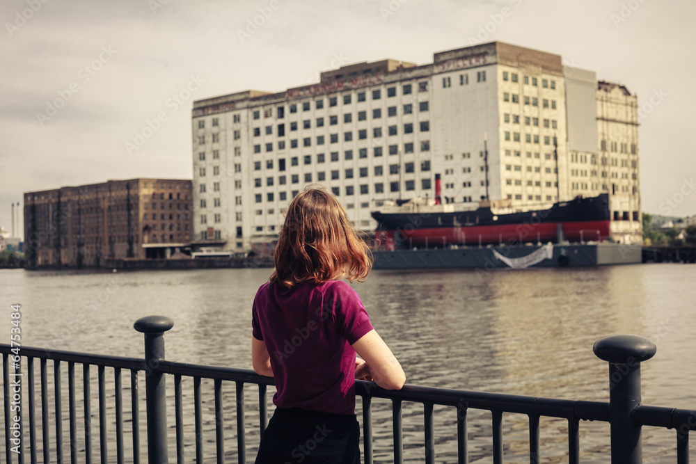 Young woman relaxing by river and looking across at buildings Young woman relaxing by river and looking across at buildings
