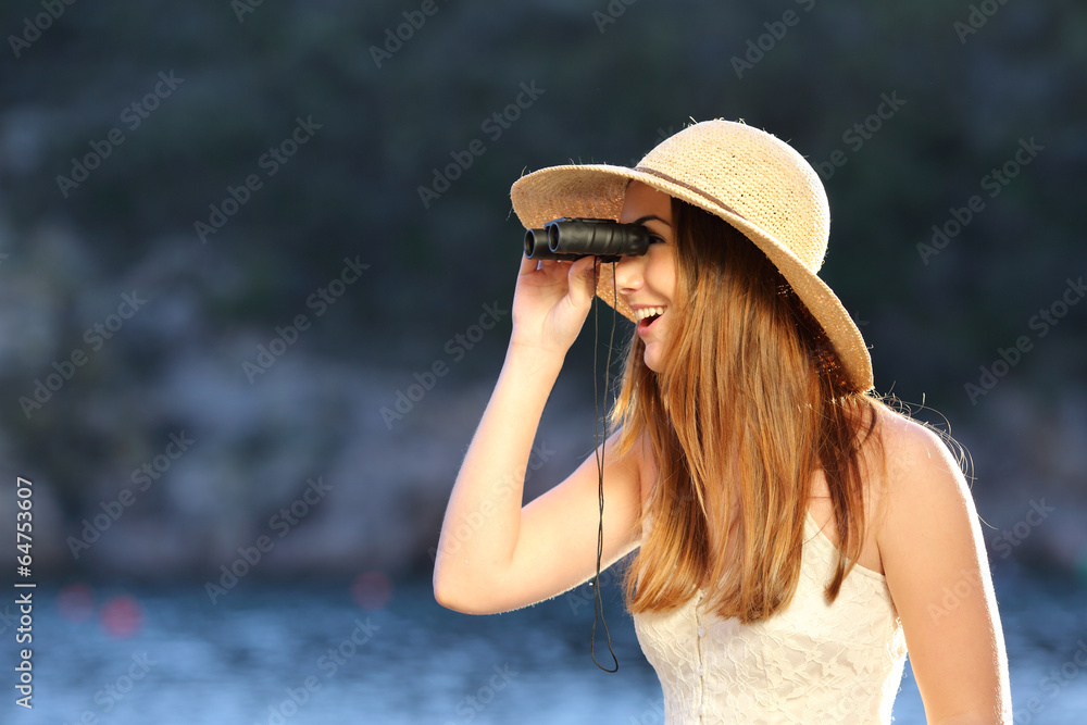 Happy woman looking through a binoculars on the beach