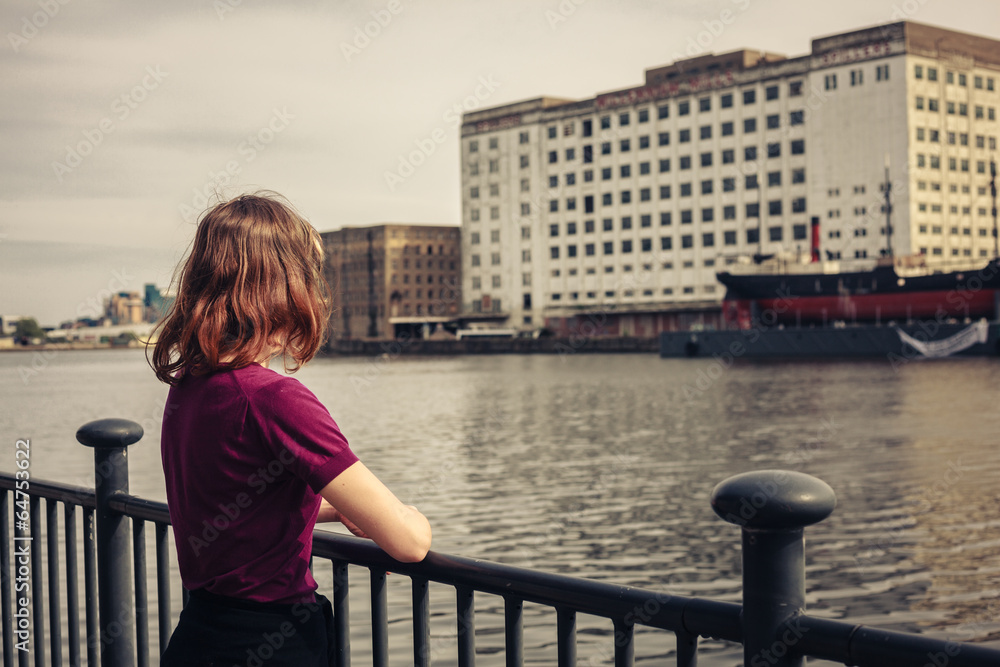 Young woman relaxing by river and looking across at buildings Young woman relaxing by river and looking across at buildings