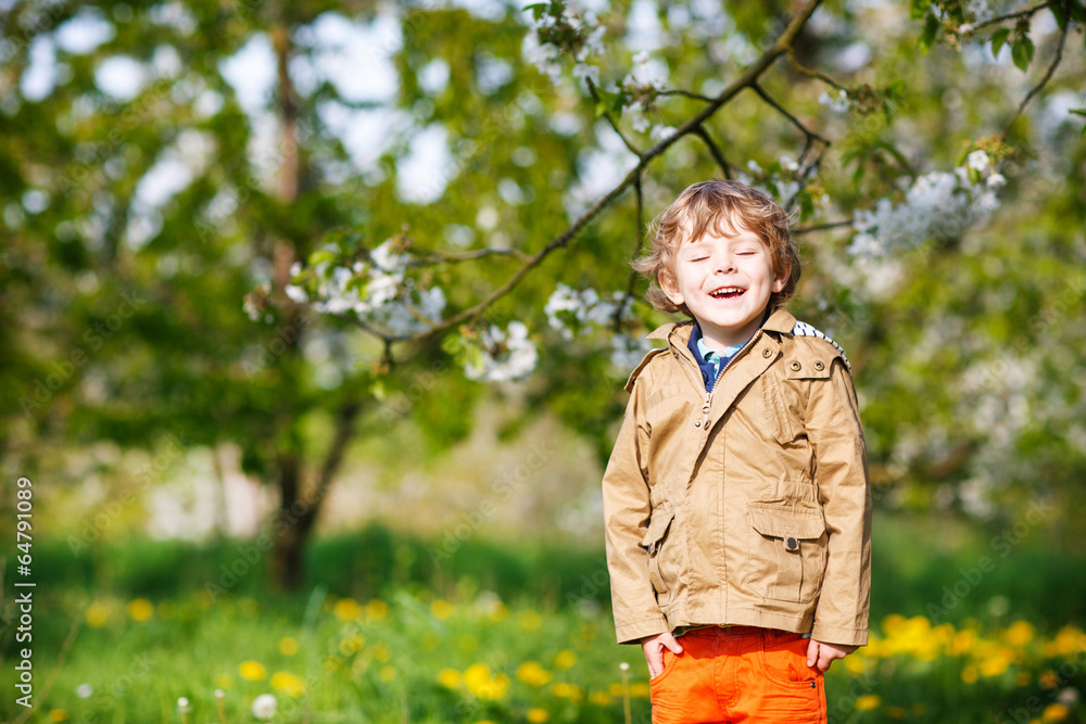 Happy little blond toddler boy in spring garden with blooming ap Happy little blond toddler boy in spring garden with blooming ap