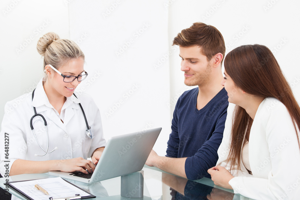 Doctor And Couple At Desk In Clinic