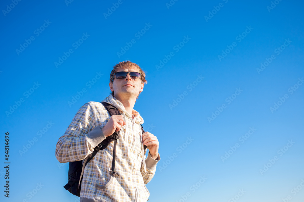 Happy man hiker holding backpack on a blue sky