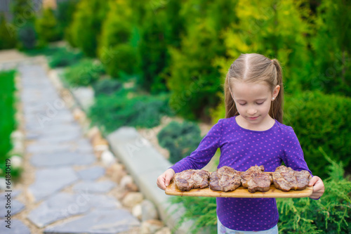 Adorable little girl with grilled steaks in the hands outdoor