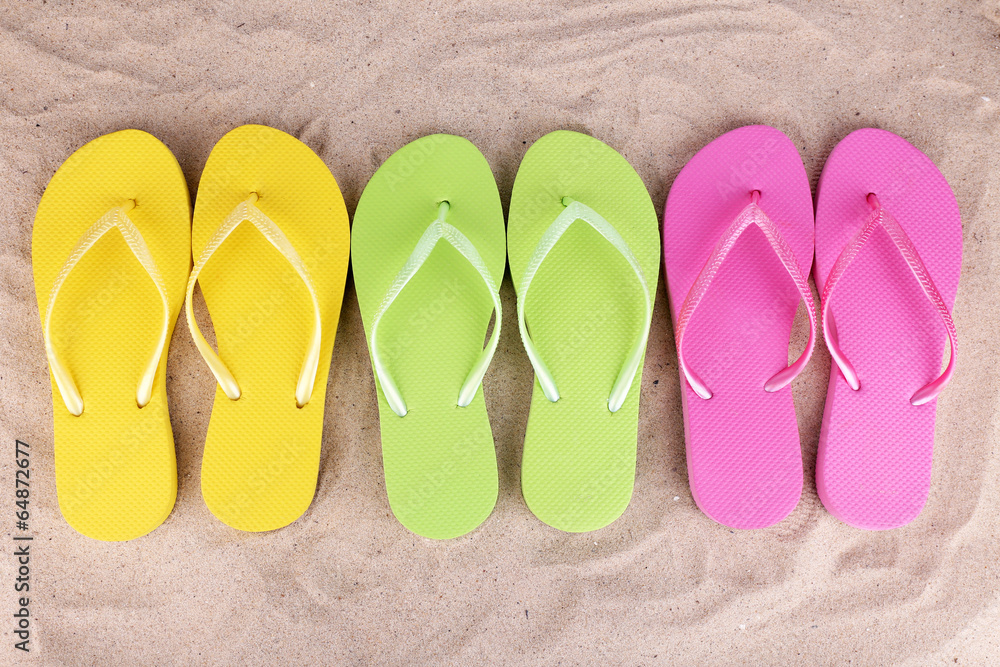 Fototapeta premium Bright flip-flops on sand, close up