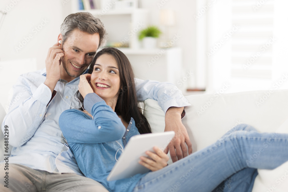 cheerful couple sharing music on digital tablet in sofa at home