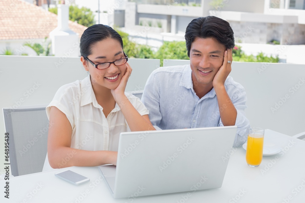 Smiling couple having breakfast together using laptop Smiling couple having breakfast together using laptop