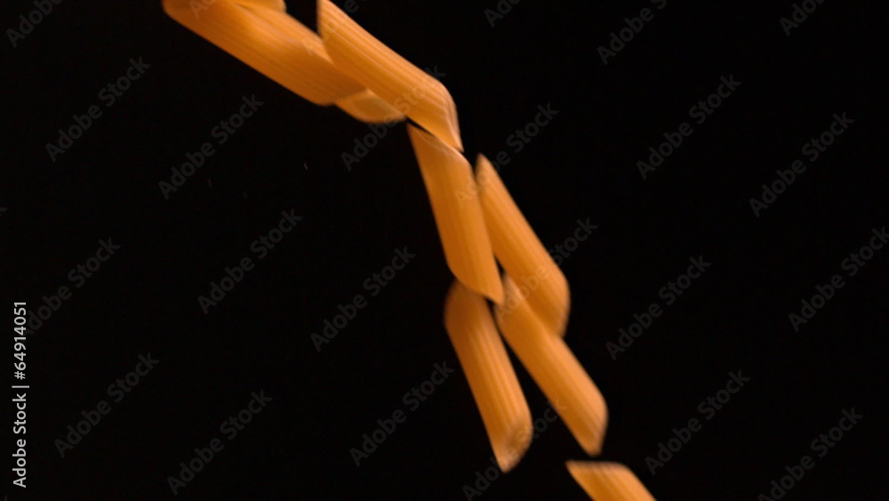 Penne pasta pouring against black background Penne pasta pouring against black background