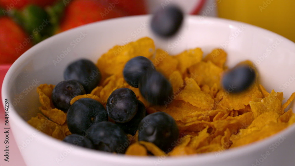 Blueberries pouring into cereal bowl at breakfast table Blueberries pouring into cereal bowl at breakfast table
