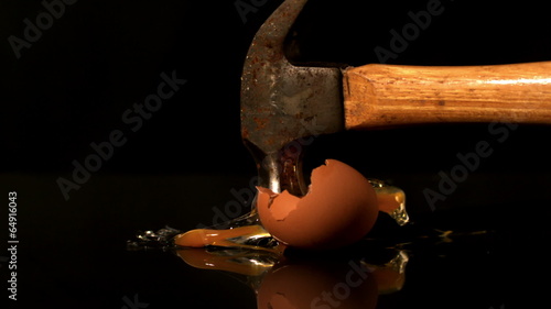 Hammer smashing egg on black background