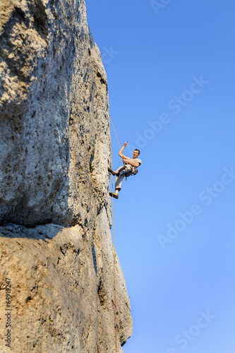 Extreme rock climbing, man on natural wall with blue sky.