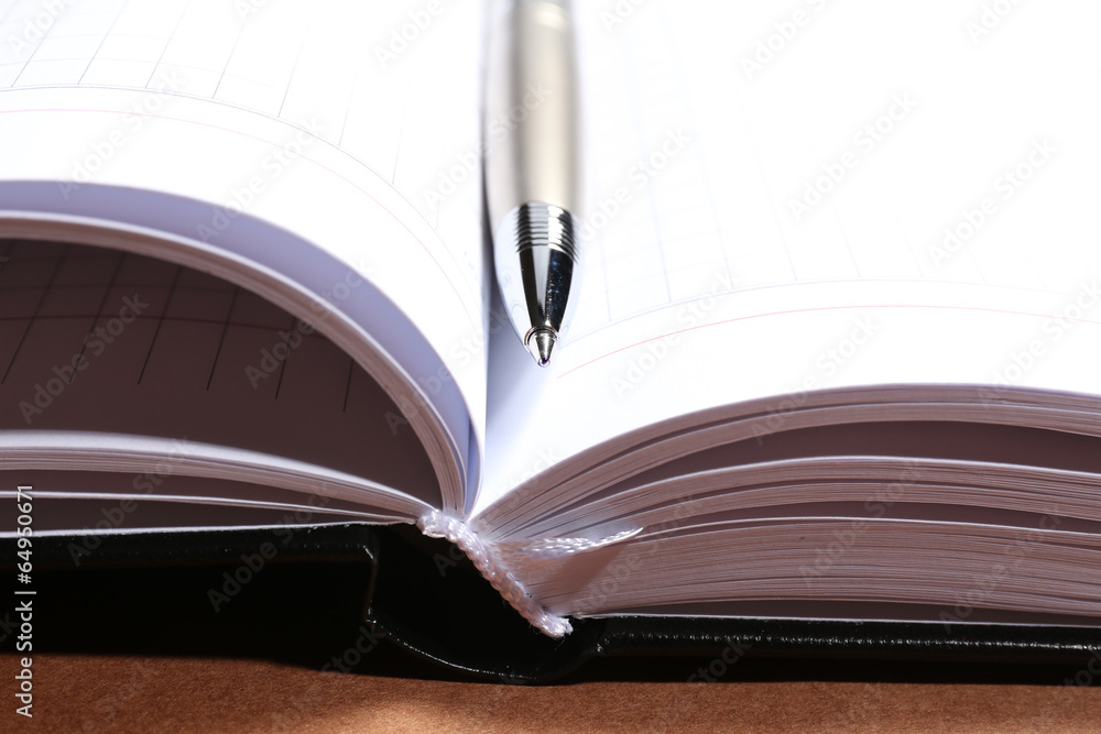 Pen on opened book on brown table Pen on opened book on brown table
