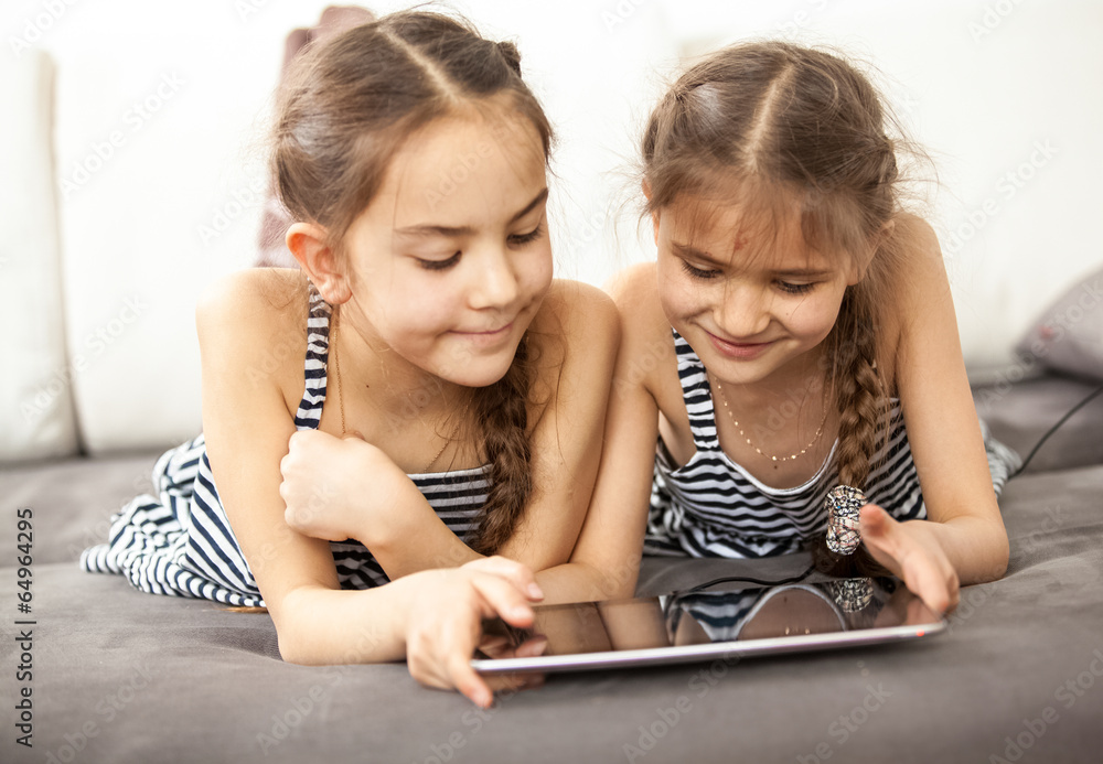 smiling schoolgirls lying on couch and playing on tablet smiling schoolgirls lying on couch and playing on tablet