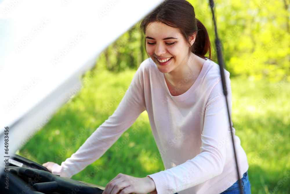 Smiling woman looks under hood car background green park