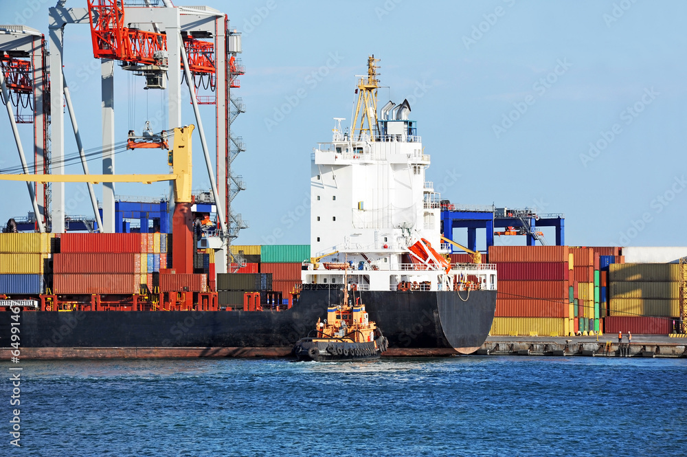 Fototapeta premium Tugboat assisting container cargo ship to harbor quayside