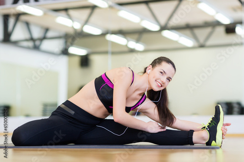 smiling girl with earphones stretching on mat