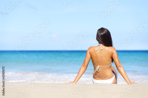 Woman on beach sitting in sand looking at ocean