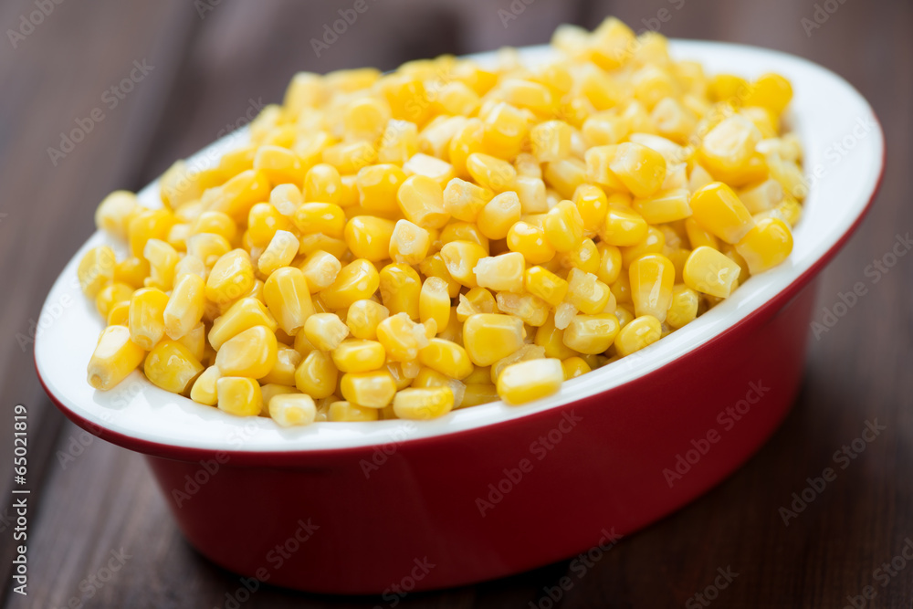 Glass bowl with corn kernels over wooden background, studio shot Glass bowl with corn kernels over wooden background, studio shot