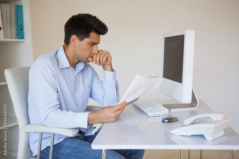 Casual businessman reading document at his desk Casual businessman reading document at his desk