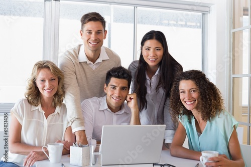 Casual smiling business team having a meeting using laptop