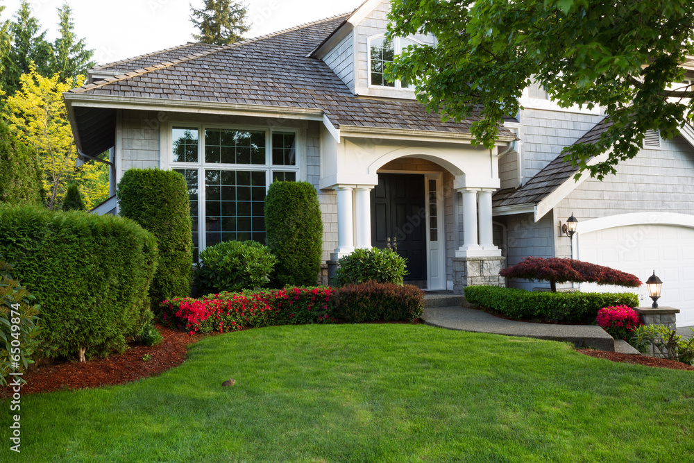 Clean exterior home with lush green grass yard, trees in bloom, and flowering bushes during spring time season  - obrazy, fototapety, plakaty 