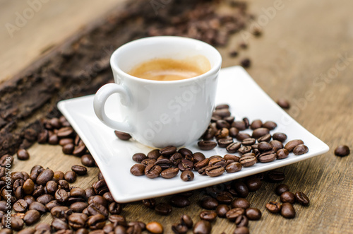 A cup of espresso and coffee beans on old wooden board