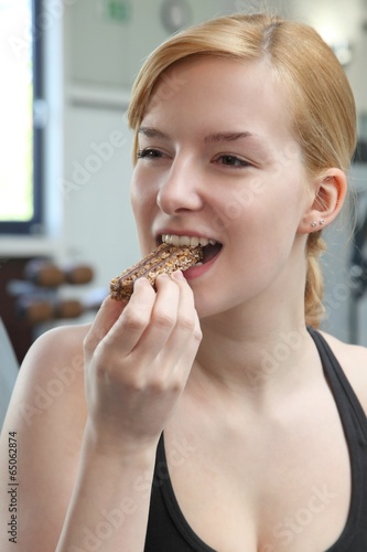 Frau isst Müsliriegel im Fitnessstudio