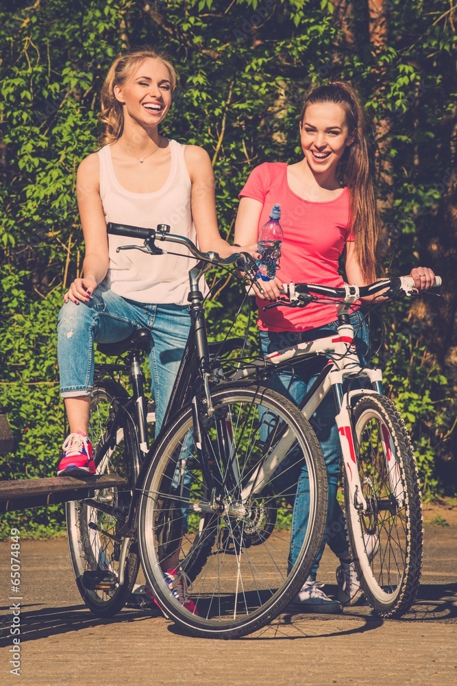 Two happy teenage girls with bicycles in a park Two happy teenage girls with bicycles in a park