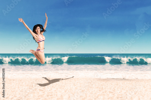 Excited woman in bikini jumping on beach