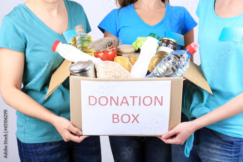 Volunteers with donation box with foodstuffs on grey background © Africa Studio