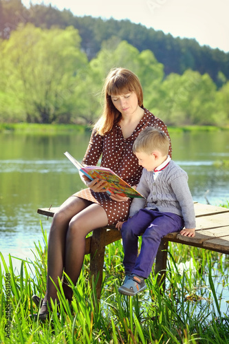 mother and son reading a book by the river