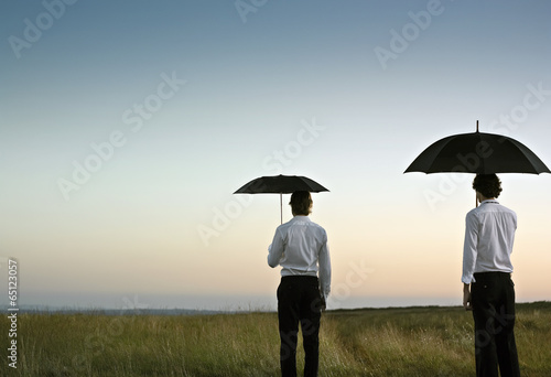 Two men with a black umbrella in an open  green field.