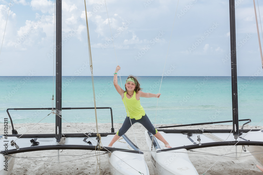 Joyful smiling yonge girl standing on catamaranon the beachy