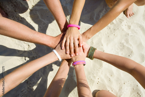 hands of young people stretching to the center on beach