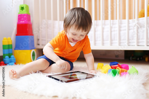 smiling 18 months baby with tablet computer at home